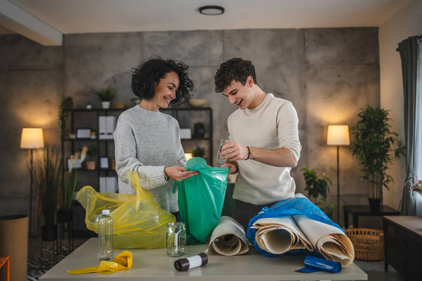 母親と息子の女性と10代の男の家族は,持続可能な生活のコンセプトを袋に廃プラスチック紙とガラスを分類する家庭でリサイクルします. - 写真・画像
