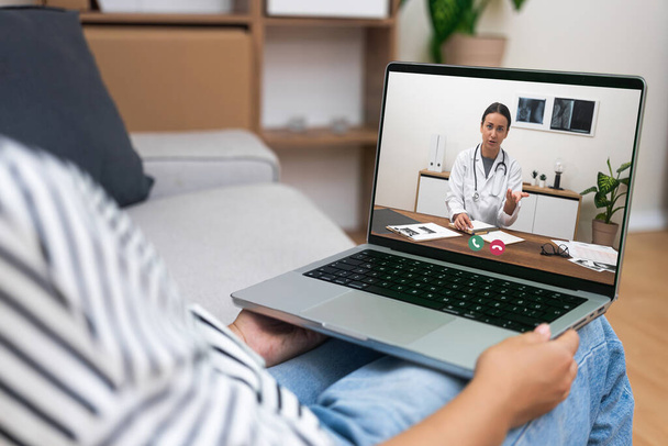 An over-the-shoulder view of a telehealth session with a doctor explaining medication to a patient via laptop. - Photo, Image