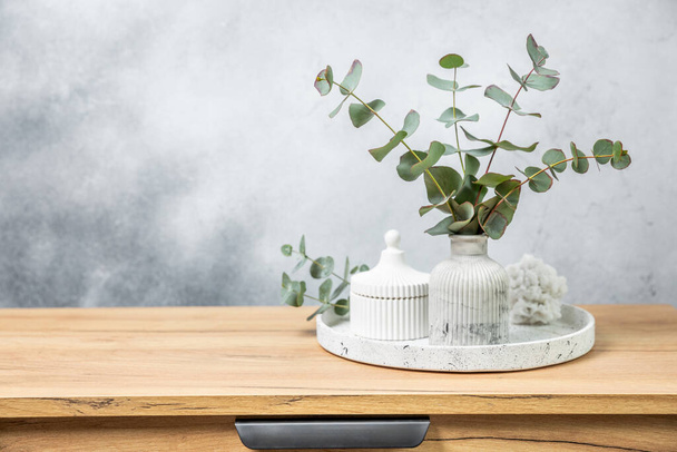 Green eucalyptus leaves in a vase stand on a chest of drawers against the background of a wall. Aromatherapy.Beautiful eucalyptus bouquet.Minimalist interior with flowers, candles and aroma diffuser. - Photo, Image