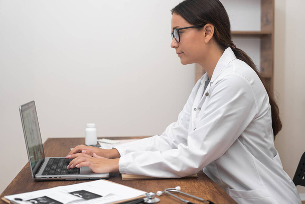 Ekspertyza telezdrowia: Kobieta lekarz, koncentruje się na laptopie, zapewnia wsparcie medyczne, prowadzi konsultacje wideo, i reprezentuje istotę telezdrowia.  - Zdjęcie, obraz