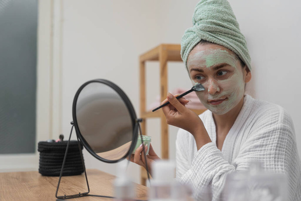 Retraite Soins de la peau : Une beauté peignoir utilise un pinceau pour appliquer un masque d'argile, admirant son reflet lors de son traitement facial bio.  - Photo, image
