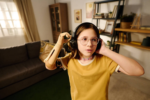 Nuorekas amputoitu tyttö tekee tanssiliikkeitä musiikkia kuulokkeet keskellä tilava olohuone nauttien vapaa - Valokuva, kuva