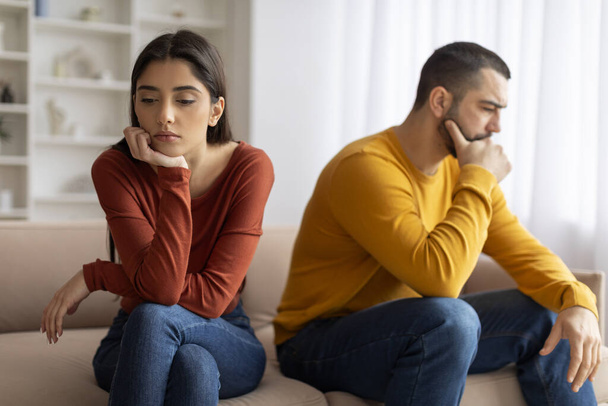Upset Young Man And Woman Offended To Each Other After Argue At Home, Pensive Millennial Spouses Sitting On Couch With Thoughtful Face Expression, Suffering Relationship Crisis After Domestic Quarrel - Photo, Image