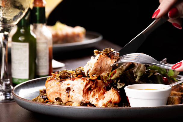 provare un piatto leggero di salmone alla griglia con insalata e brindare con vino bianco mano femminile in primo piano - Foto, immagini