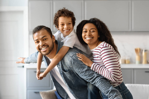 Портрет веселого чорного сімейства з маленьким сином посміхається на камеру, щасливі афроамериканські батьки зв'язуються зі своїм п'ятнадцятьма сином, позуючи разом в домашньому інтер'єрі - Фото, зображення