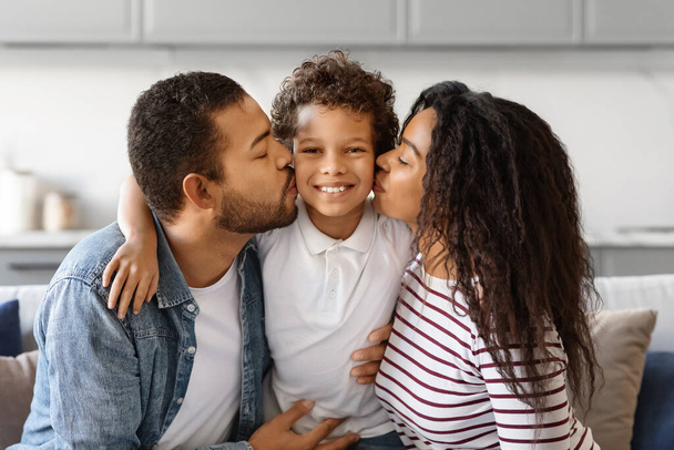 Boldog családi portré. Szoros lövés szerető fekete szülők csókolgatja a kaméleon fia, aranyos férfi gyermek mosolygott a kamera, fiatal afro-amerikai anya és apa kötődik a gyerek otthon - Fotó, kép