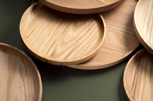 Fa lapos lemezek sötétzöld háttérrel. Az ökológiai evőeszközök fogalma. A modern konyha termékei. Természetes harmónia: fa tányérok egy környezetbarát konyhában. Meleg lámpaernyők. - Fotó, kép