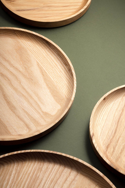 Wooden flat plates on a dark green background. The concept of ecological tableware. Products for modern kitchen. Natural harmony: wooden plates in an eco-friendly kitchen. Warm lamp shades. - Photo, Image
