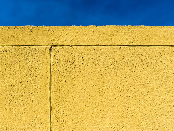 eine gelbe Zementwand mit blauem Himmel im Hintergrund - Foto, Bild