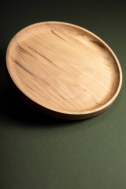 Fa lapos lemezek sötétzöld háttérrel. Az ökológiai evőeszközök fogalma. A modern konyha termékei. Természetes harmónia: fa tányérok egy környezetbarát konyhában. Meleg lámpaernyők. - Fotó, kép