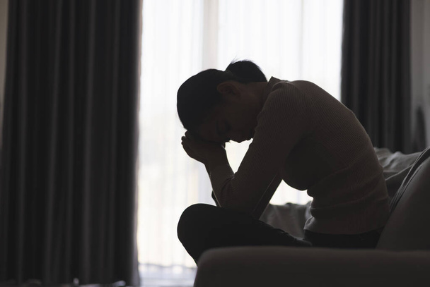 Silueta osoby trpící depresí v domě, depresivní žena sedí sama na pohovce cítit stres, smutný a ustaraný v temné místnosti. osoba jsou ve stresu. - Fotografie, Obrázek