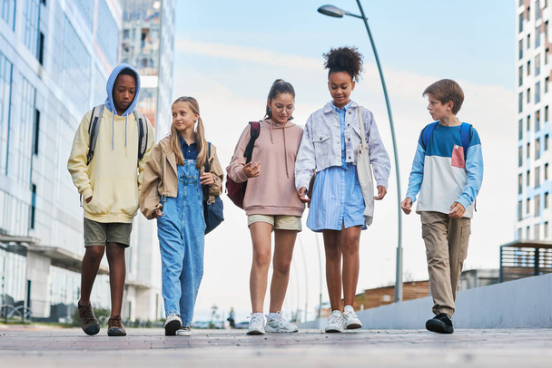 Rivi monikulttuurisia nuoria rennoissa vaatteissa kävelemässä kadulla ja puhumassa toisilleen tullessaan koulusta kotiin. - Valokuva, kuva