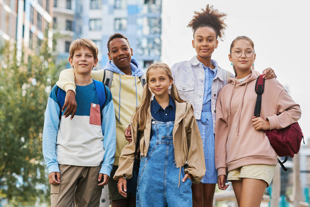 Öt multikulturális középiskolai tanulóból álló csoport alkalmi viseletben, akik sorban állnak városi környezetben és kamerába néznek - Fotó, kép