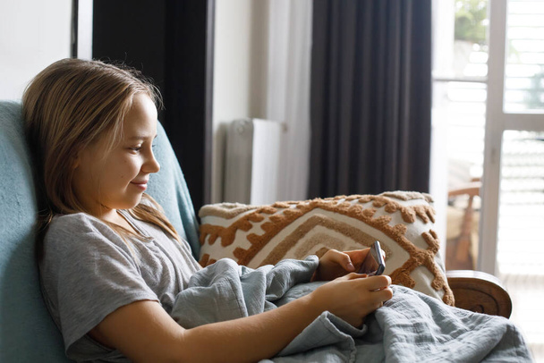 Ein Kind sitzt in ihrem Zimmer und hat Spaß beim Spielen auf ihrem Smartphone - Foto, Bild