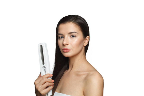 Гарна модель жінки, що тримає залізо для волосся і випрямляє її здорове довге темне волосся, ізольоване на білому тлі. Концепція укладання волосся та волосся - Фото, зображення