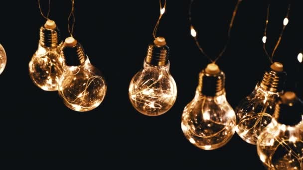 Sok akasztás izzó Vintage Edison villanykörték fekete háttér. Első látásra. Meleg fény. Textúra, szerkezet. Evezz! Dekoratív évjárat elektromos izzók, retro stílusú koszorú világítja meg a teret. - Felvétel, videó