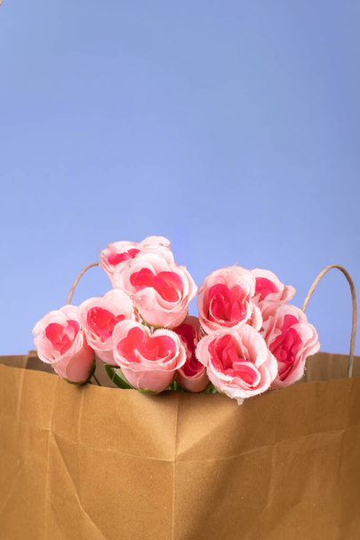 Μπουκέτο ροζ τριαντάφυλλα σε χάρτινη σακούλα σε μπλε φόντο - Φωτογραφία, εικόνα