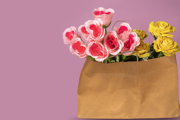 Μπουκέτο ροζ και κίτρινες τουλίπες σε καφέ χάρτινη σακούλα σε μωβ φόντο με χώρο αντιγραφής για το κείμενό σας - Φωτογραφία, εικόνα