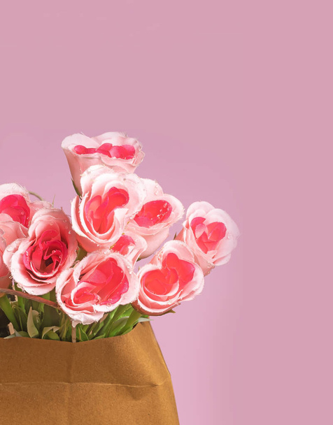 Un ramo de rosas rosadas artificiales en una bolsa de papel marrón sobre un fondo rosado con espacio para copiar - Foto, Imagen