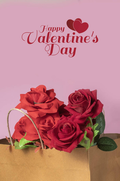 Tarjeta de felicitación de San Valentín con rosas rojas en una bolsa de papel sobre fondo rosa - Foto, Imagen