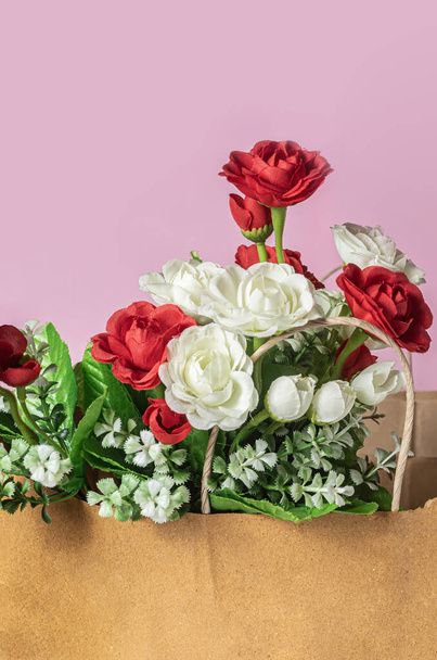 Ein Strauß roter und weißer Rosen in einer Papiertüte auf rosa Hintergrund - Foto, Bild