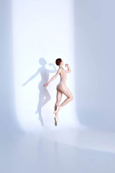 Élégance athlétique. Full-Length Portrait de danseuse gracieuse porte un maillot de bain sport rose et des chaussures pointes, se déplaçant avec flexibilité contre studio blanc. Concept de ballet, athlétisme, grâce. - Photo, image