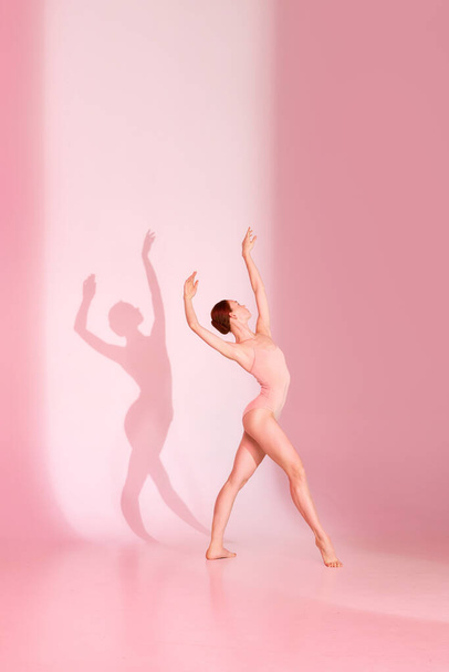 Пошепки Благодать. Балерина в рожевому вбранні танцює на м'якому фоні, її тінь імітує кожен хід. Концепція мистецтва і балету, грація і краса, плинність, танець тіней. - Фото, зображення