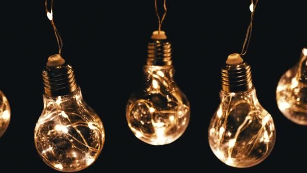 Lots Hanging Glowing Vintage Edison Light Bulbs on Black Background. Top view. Warm light. Texture, structure. Row. Decorative vintage electric light bulbs, retro style garland illuminate the space. - Footage, Video
