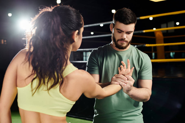 Ένας άνδρας εκπαιδευτής διδάσκει τεχνικές αυτοάμυνας σε μια γυναίκα σε ένα γυμναστήριο, καθώς στέκονται δίπλα-δίπλα.. - Φωτογραφία, εικόνα