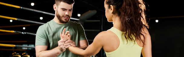 Un entrenador masculino demuestra técnicas de autodefensa a una mujer en un entorno de gimnasio. - Foto, Imagen
