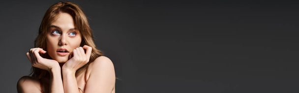Attractive surprised young woman with blue eyes, posing on dark grey background, banner. Peach fuzz - Photo, Image