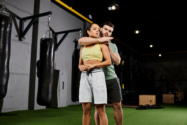 Een mannelijke trainer begeleidt een vrouw in het beheersen van zelfverdedigingstechnieken in een sportschool, toont kracht en empowerment. - Foto, afbeelding
