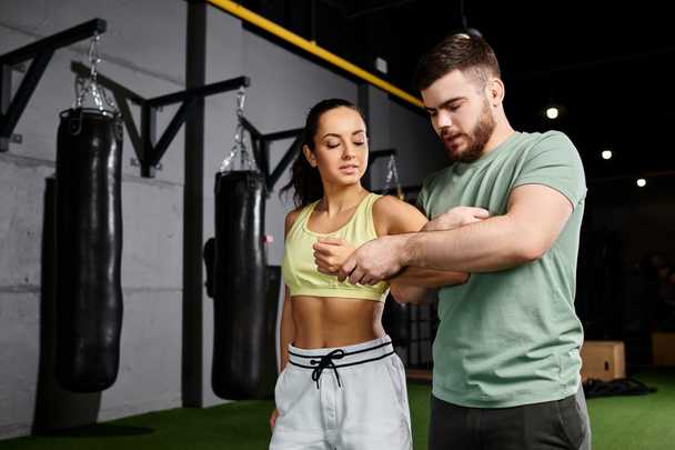 Ένας άνδρας εκπαιδευτής εκπαιδεύει μια γυναίκα σε τεχνικές αυτοάμυνας, στέκεται μαζί σε ένα γυμναστήριο. - Φωτογραφία, εικόνα