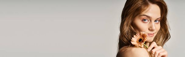 Oldalnézet mosolygós vonzó lány, gerbera százszorszép közel arc szürke háttér, banner - Fotó, kép