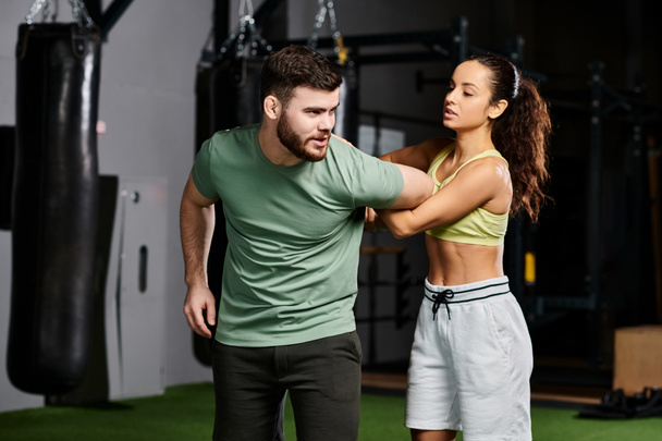 Un entrenador masculino está enseñando hábilmente técnicas de autodefensa a una mujer en un gimnasio moderno lleno de equipos de fitness. - Foto, Imagen