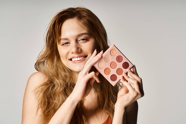 Beauty shot of smiling woman holding nude eyeshadow palette near face and looking at camera - Photo, Image