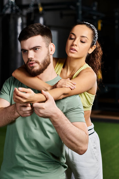 Een man die zelfverdedigingstechnieken demonstreert aan een vrouw in een fitnessruimte. - Foto, afbeelding
