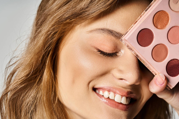 Closeup studio beauty shot of smiling woman with peach makeup palette near face with closed eyes - Foto, immagini