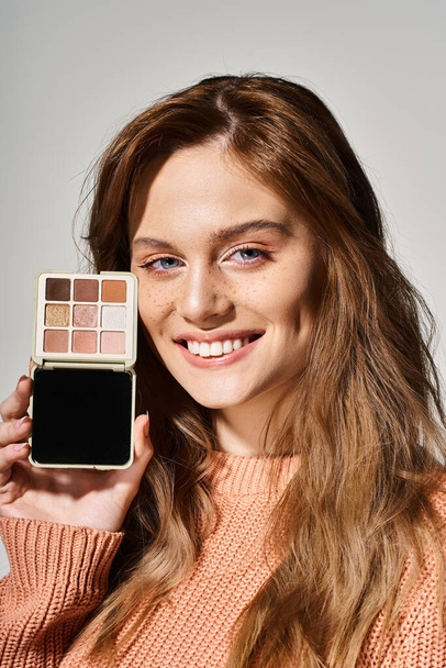 Lachende mooie aantrekkelijke vrouw met perzik make-up palet in de buurt gezicht op grijze studio achtergrond - Foto, afbeelding