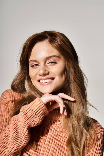 Portrait of smiling woman looking at camera with natural makeup, wearing sweater, touching her chin - Fotografie, Obrázek