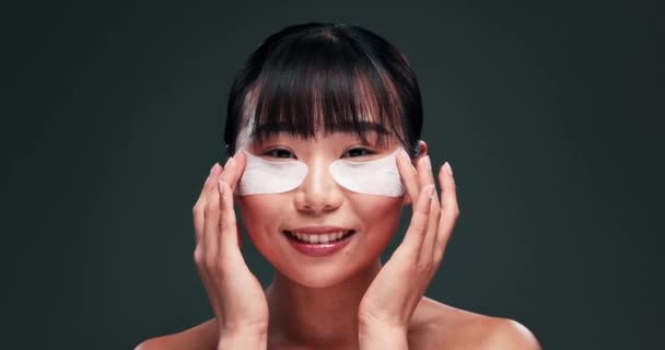 Skincare, eye pad e viso di donna asiatica in studio con retinolo prodotto, viso e beauty routine. Sorriso, benefici cosmetici e ragazza con patch di collagene per dermatologia su sfondo verde scuro - Filmati, video