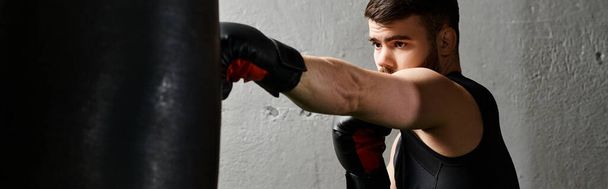 A handsome man with a beard fiercely boxing in a gym with a red punching bag wearing a black shirt. - Photo, Image