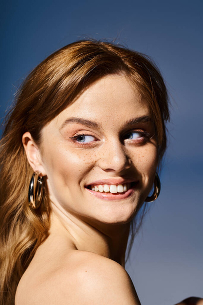 Genç, güzel, gülümseyen bir kadın mavi arka planda doğal şeftali makyajıyla yüzünü çeviriyor. - Fotoğraf, Görsel