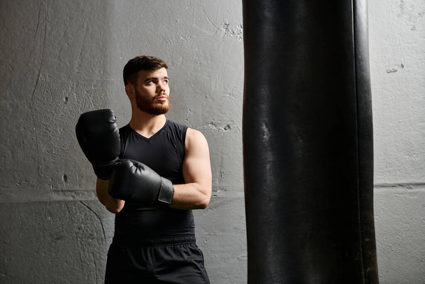 A handsome man with a beard stands next to a punching bag in a gym, practicing boxing. - Photo, Image