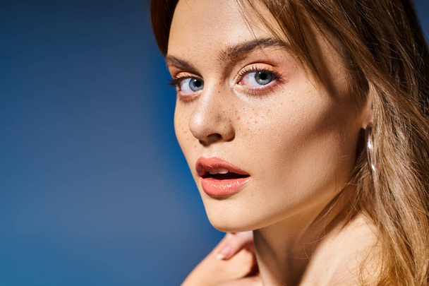 Closeup side view photo of girl with blue eyes, peach nude makeup with freckles on blue background - Fotoğraf, Görsel