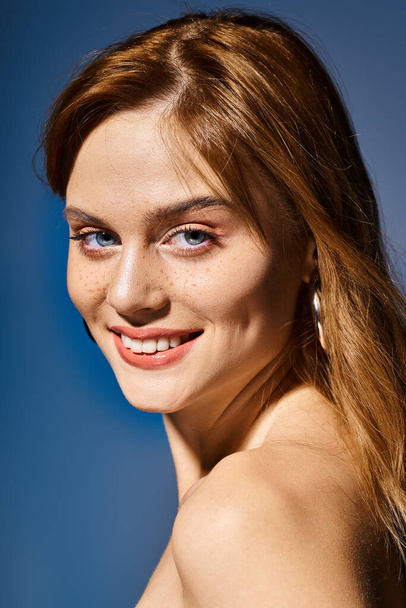 Vista lateral de chica sonriente con ojos azules, maquillaje desnudo melocotón con pecas sobre fondo azul - Foto, Imagen