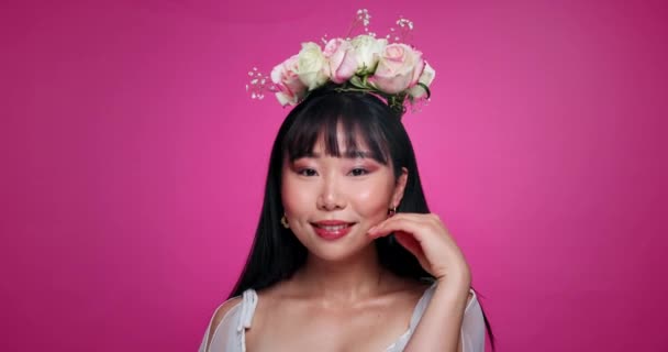 Růžové pozadí, make-up a tvář asijské ženy s květinovou korunou pro wellness, luxus a úsměv. Salon, květinová estetika a portrét člověka pro přírodní krásu, kosmetiku a péči o pleť ve studiu. - Záběry, video