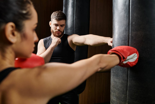 Ein männlicher Trainer coacht eine brünette Sportlerin in aktiver Kleidung bei einem kraftvollen Boxtraining in einem Fitnessstudio. - Foto, Bild