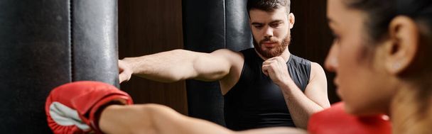 Тренер-мужчина поддерживает брюнетку-спортсменку в активной одежде, когда они дерутся в боксёрском ринге в спортзале. - Фото, изображение