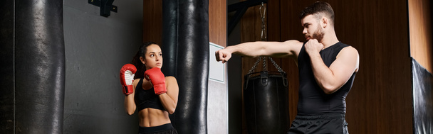 A male trainer supports a brunette sportswoman as they spar in a boxing ring in a gym. - Photo, Image